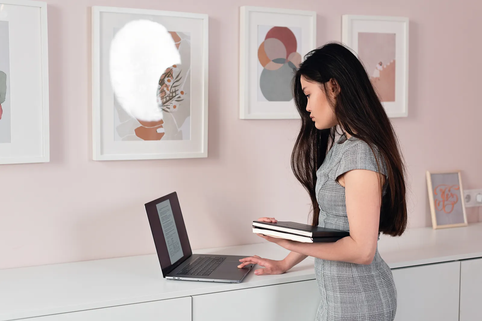 A businesswoman stands indoors, using a laptop, reflecting focus and professionalism