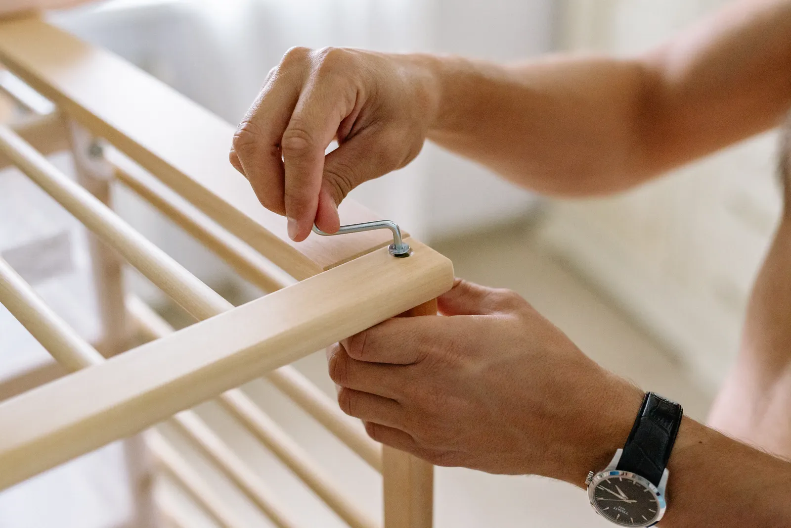 Close-up of a man using an Allen wrench to assemble a wooden baby cot indoors