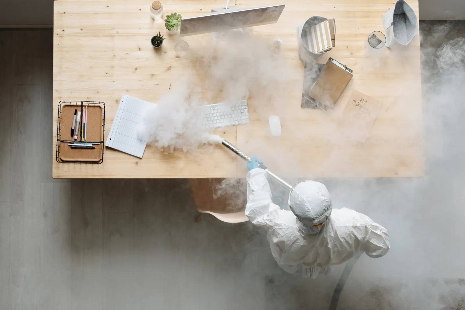 An individual disinfects a workspace using fumigation, wearing full protective gear for safety