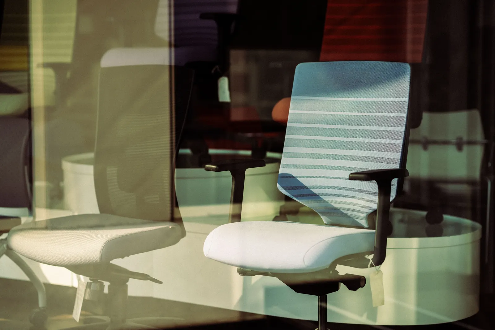 Contemporary office chairs displayed behind glass, offering modern ergonomic solutions for workspace